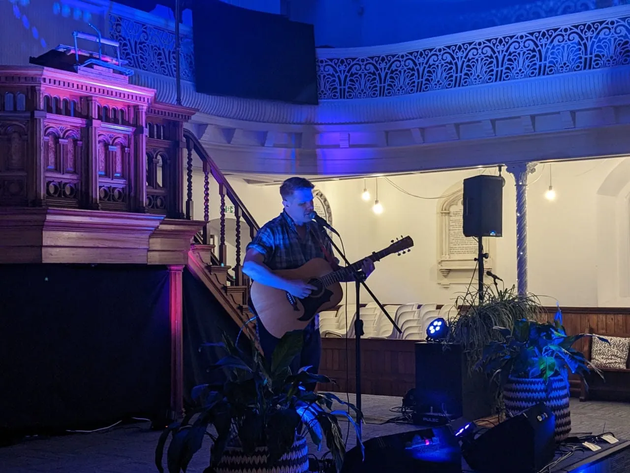 A man playing guitar in a church with blue lighting. Adam singing a live gig.