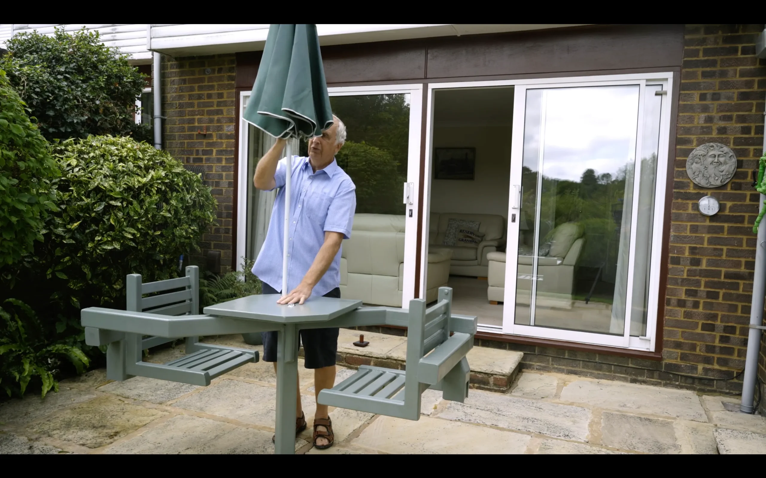 Man setting up umbrella on outdoor table on patio.