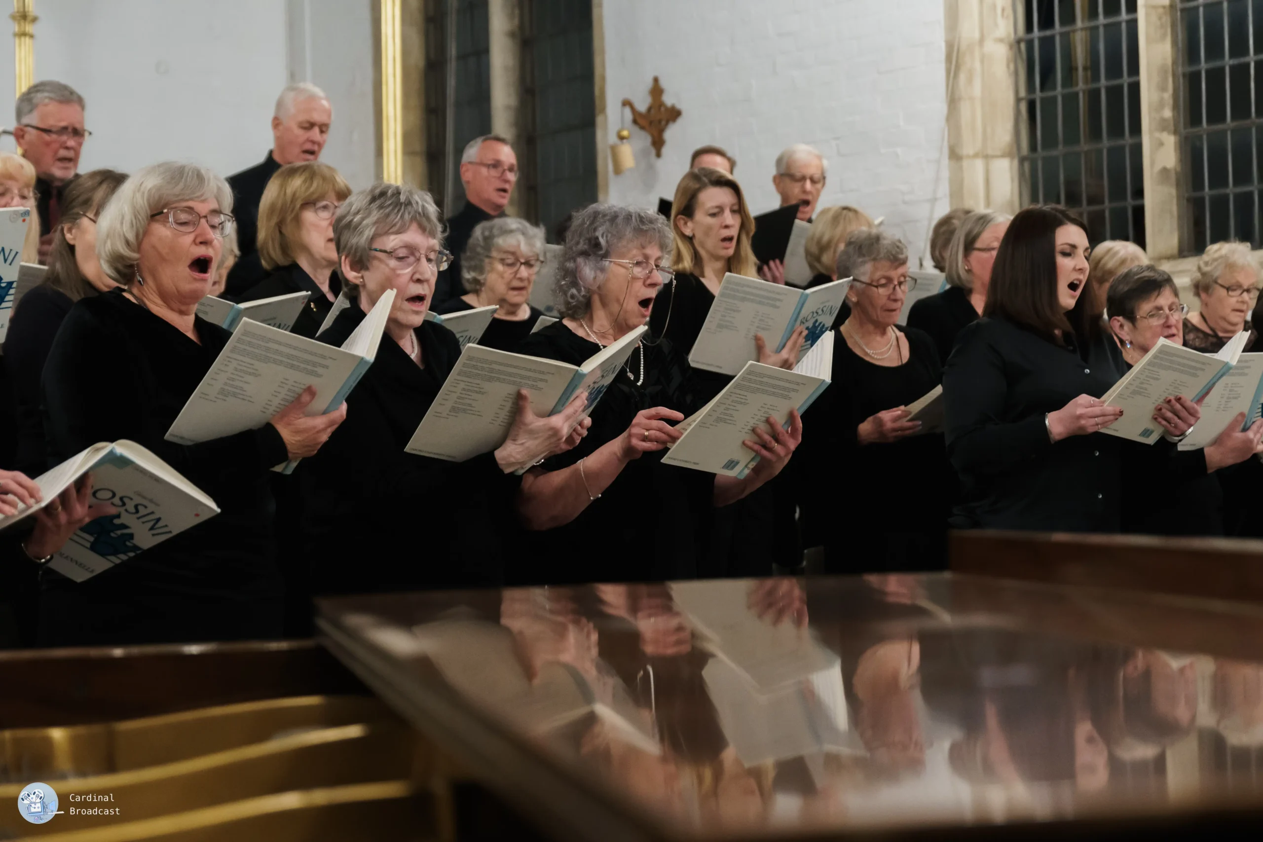 Group of chorus members standing behind a piano, singing in harmony.