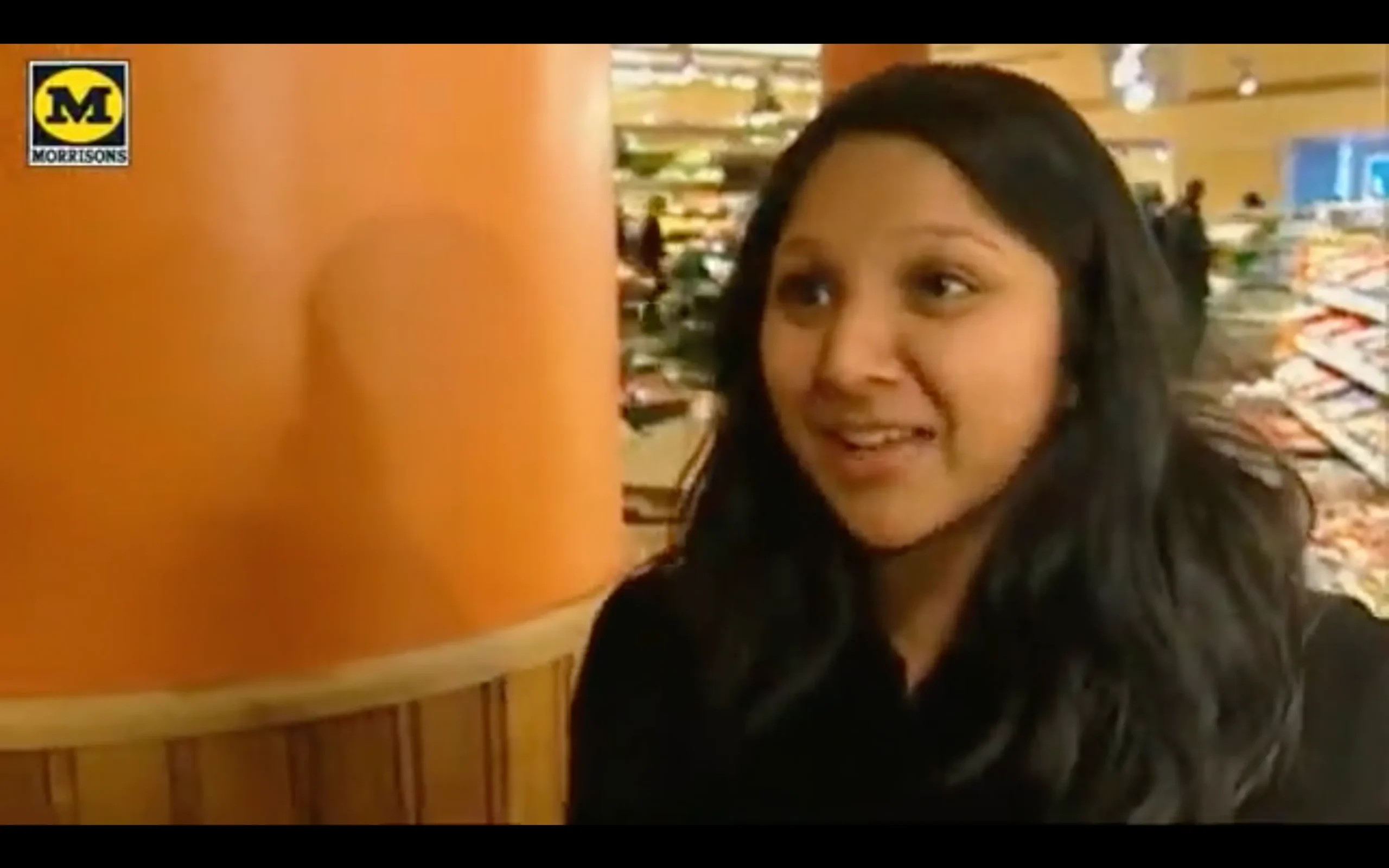 A woman in a supermarket engaging with the camera, discussing her personal experience.