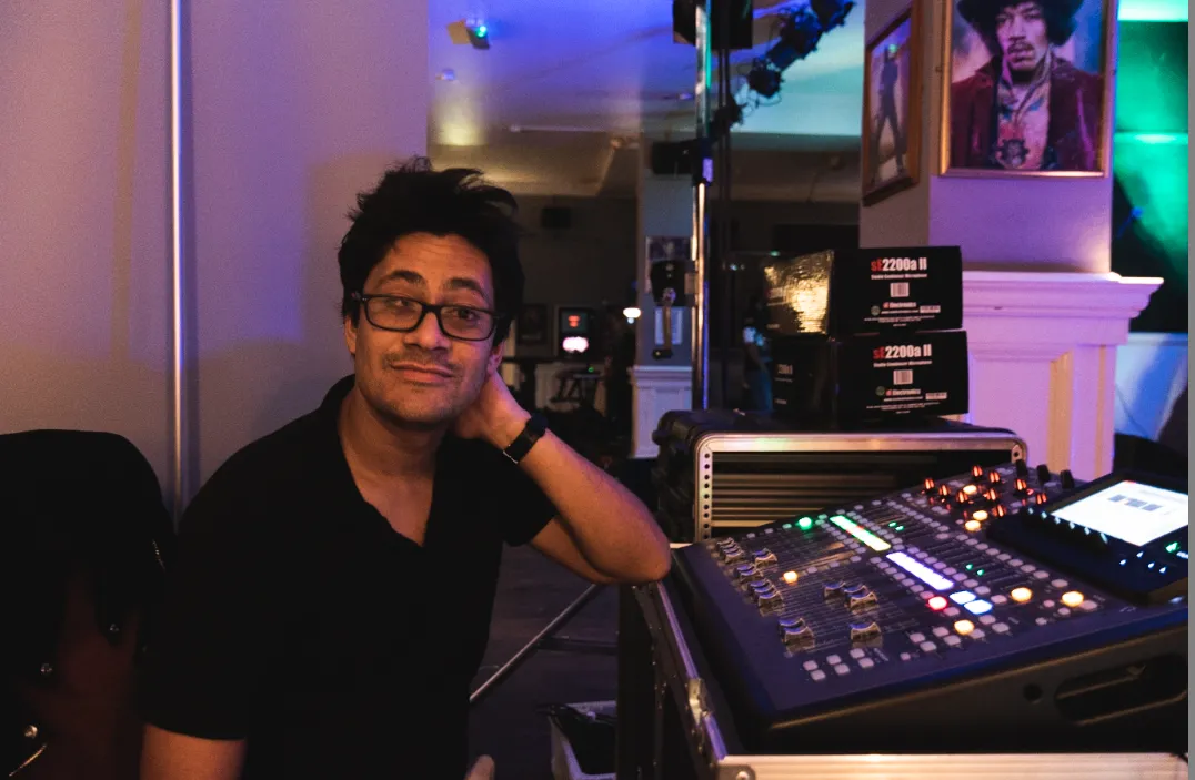 A man in glasses sits at a Sound Desk, focused on a mixer.