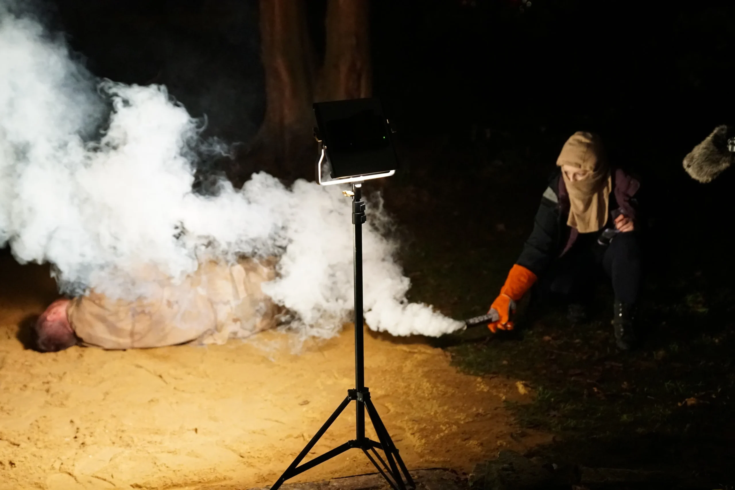 A person cover up while using a smoke grande, while a person on the ground is enveloped in smoke from above.