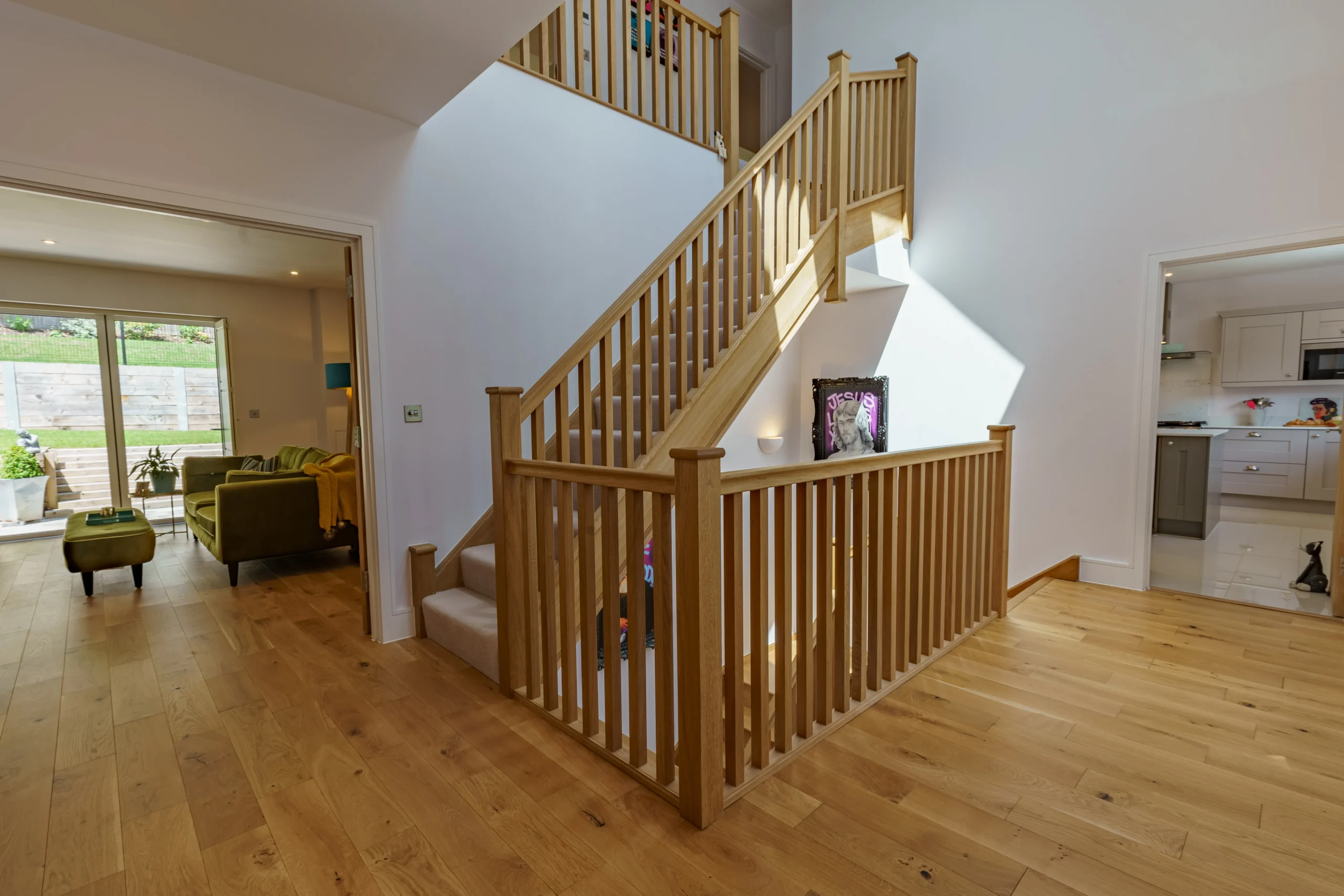 Inside the house is a wooden staircase leading to a landing, with white walls in the living room.