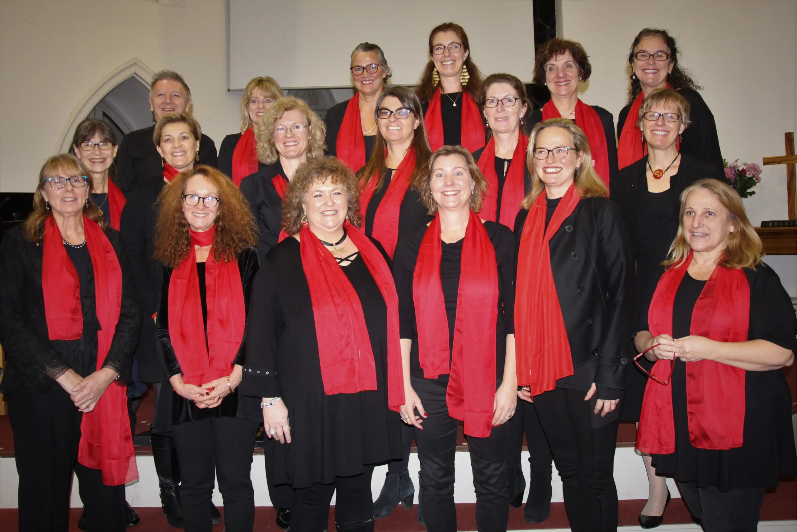 A choir of women wearing black and red scarves, harmoniously singing together in perfect unison.