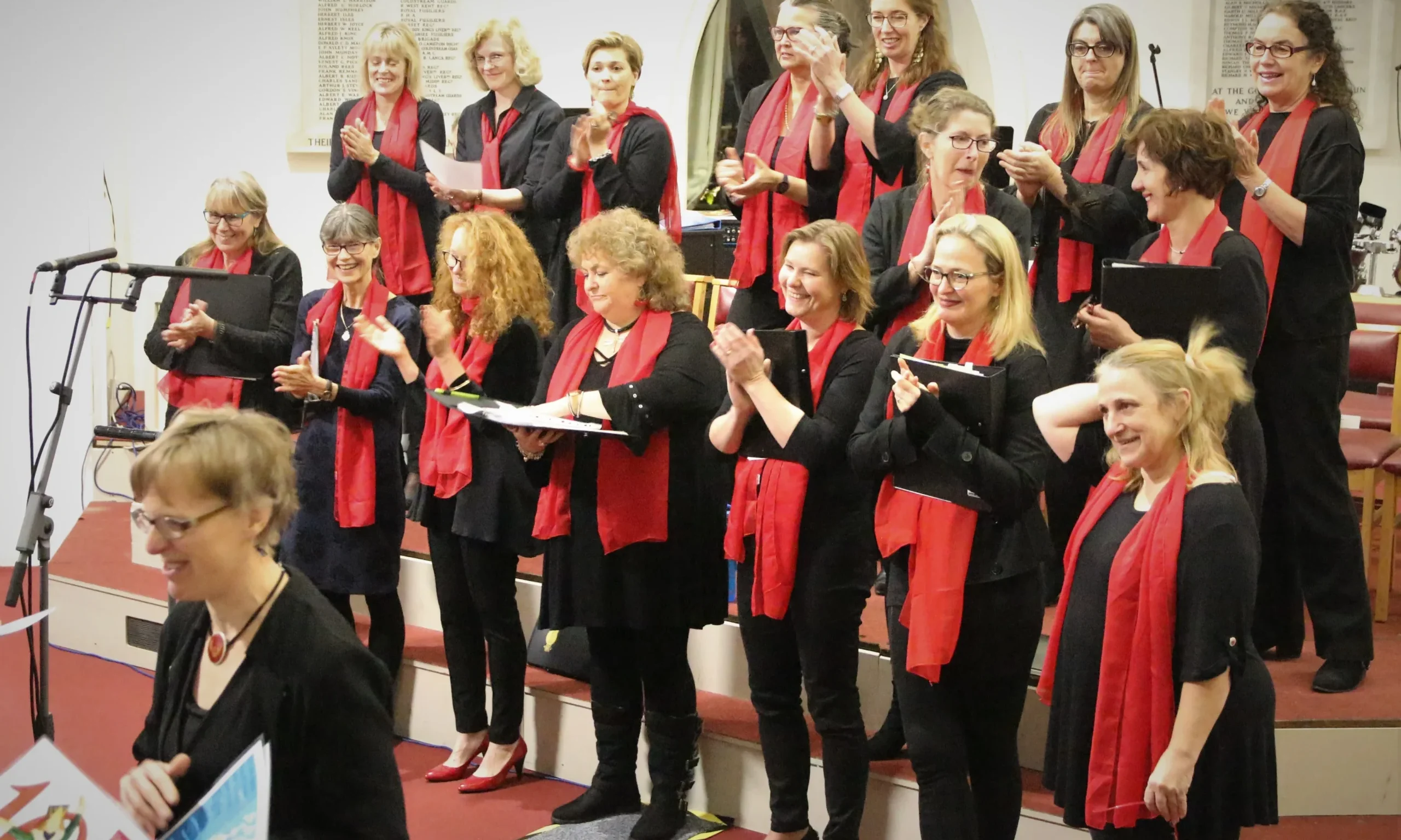 Group of female singers in red and black attire harmonizing together.